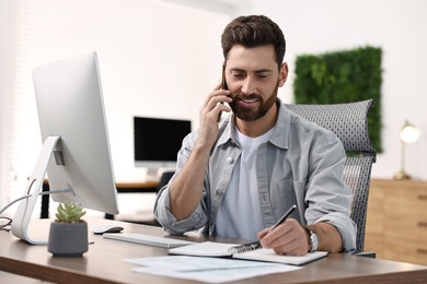 Man talking on smartphone while working at table in office