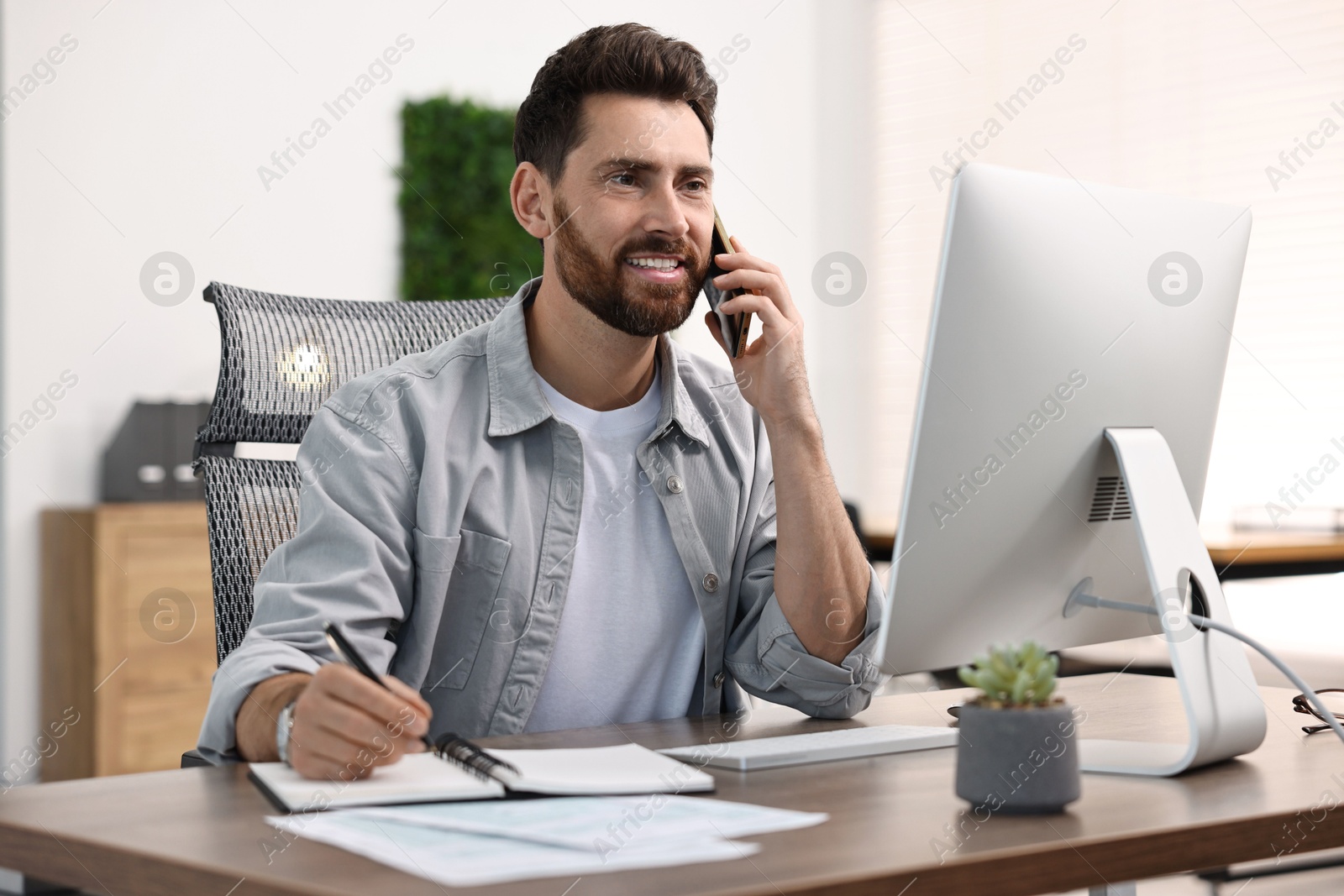 Photo of Man talking on smartphone while working at table in office