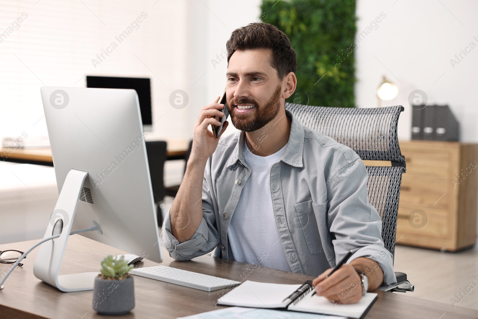 Photo of Man talking on smartphone while working at table in office