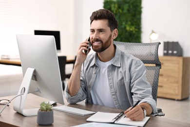 Photo of Man talking on smartphone while working at table in office