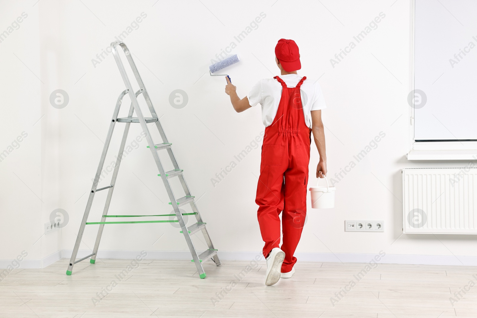 Photo of Handyman painting wall with roller indoors, back view