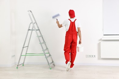 Photo of Handyman painting wall with roller indoors, back view