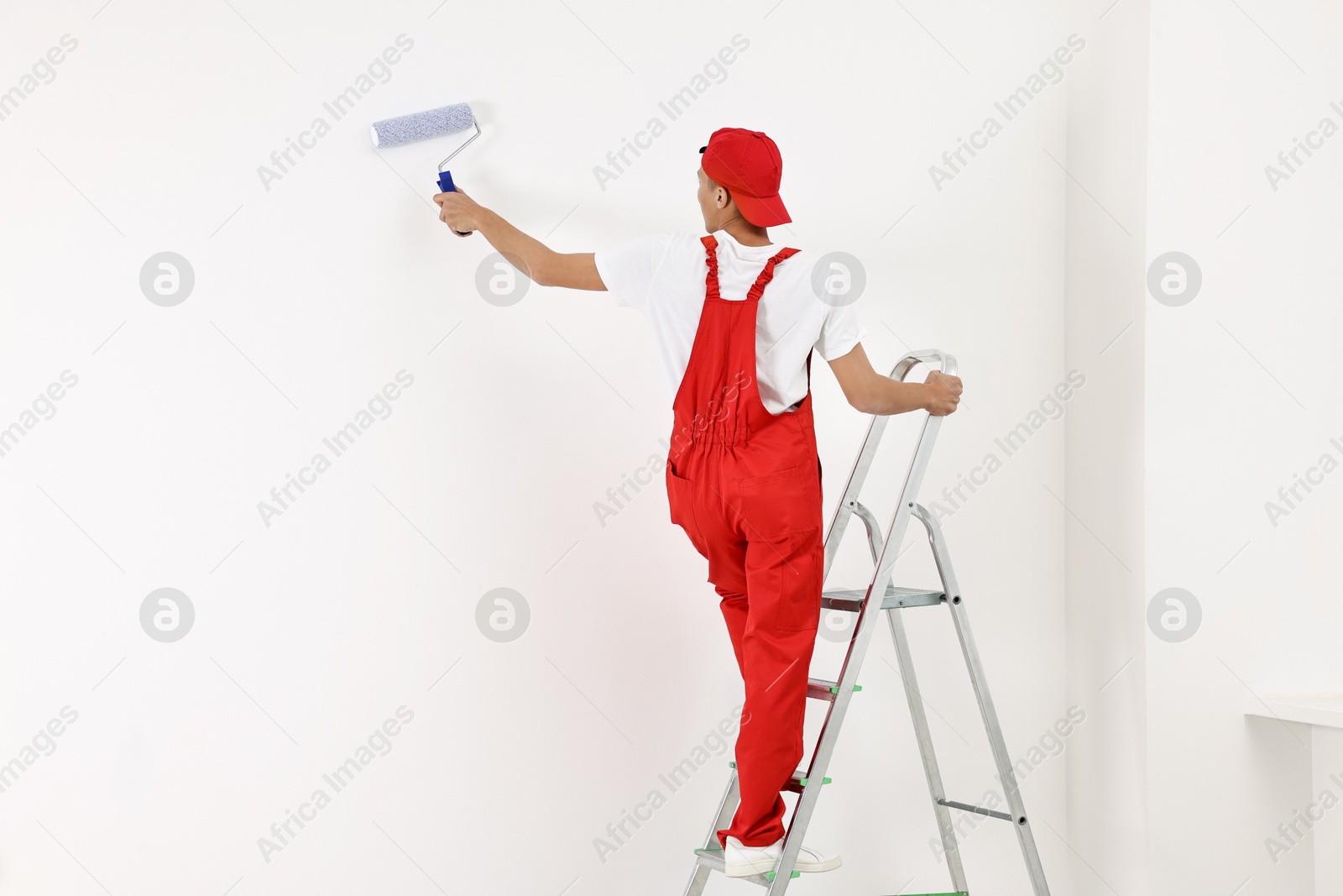 Photo of Handyman painting wall with roller indoors, back view