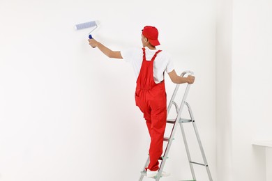 Photo of Handyman painting wall with roller indoors, back view