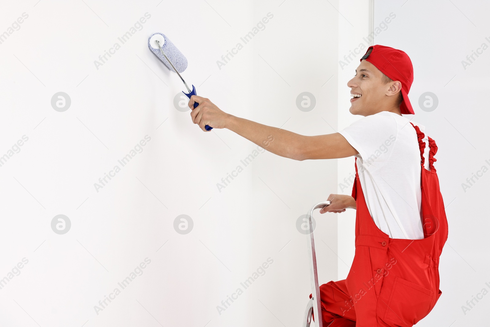 Photo of Smiling handyman painting wall with roller indoors. Space for text