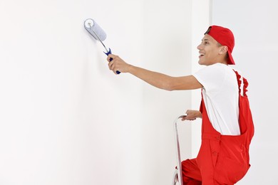 Photo of Smiling handyman painting wall with roller indoors. Space for text