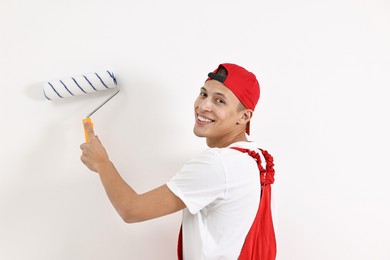 Photo of Smiling handyman painting wall with roller indoors