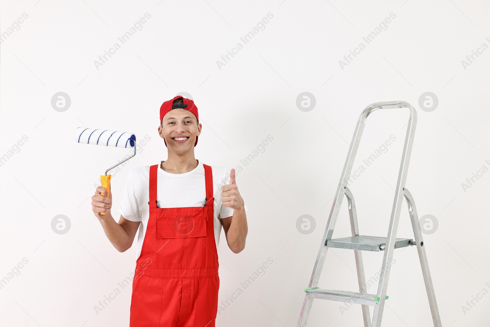 Photo of Smiling handyman with paint roller showing thumbs up indoors