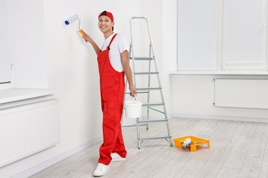 Photo of Smiling handyman painting wall with roller indoors