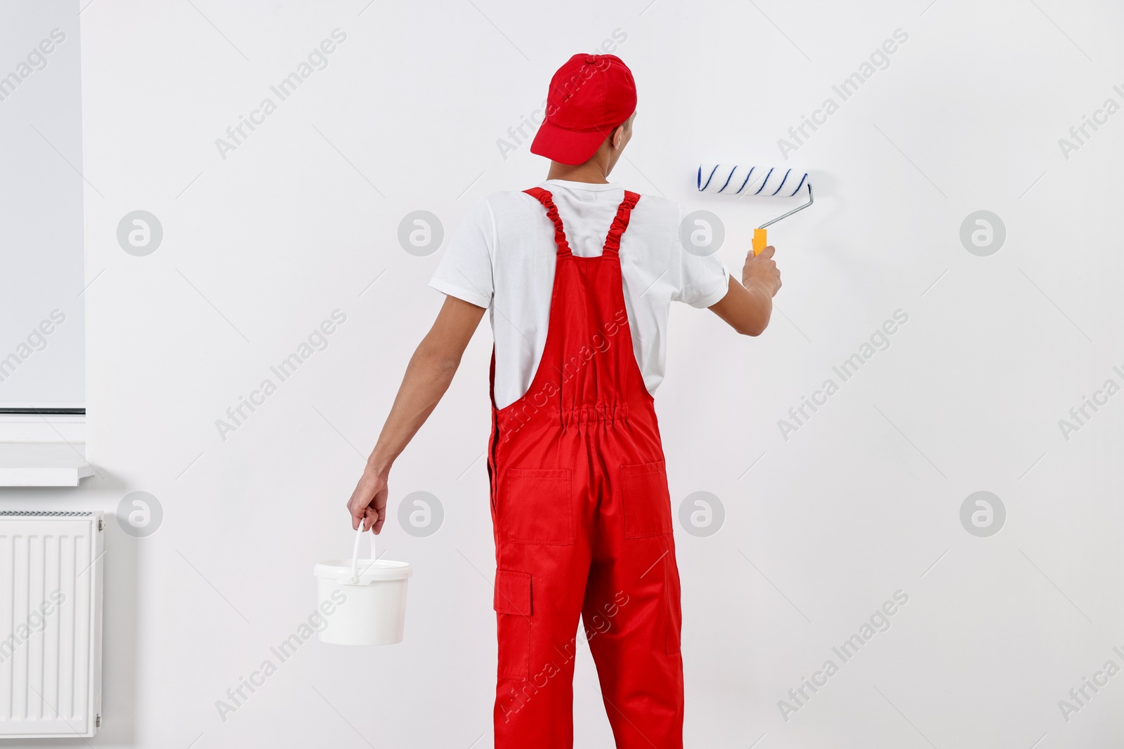 Photo of Male handyman painting wall with roller indoors, back view