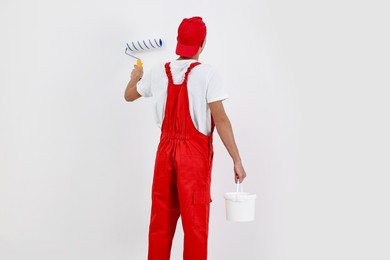 Photo of Male handyman painting wall with roller indoors, back view