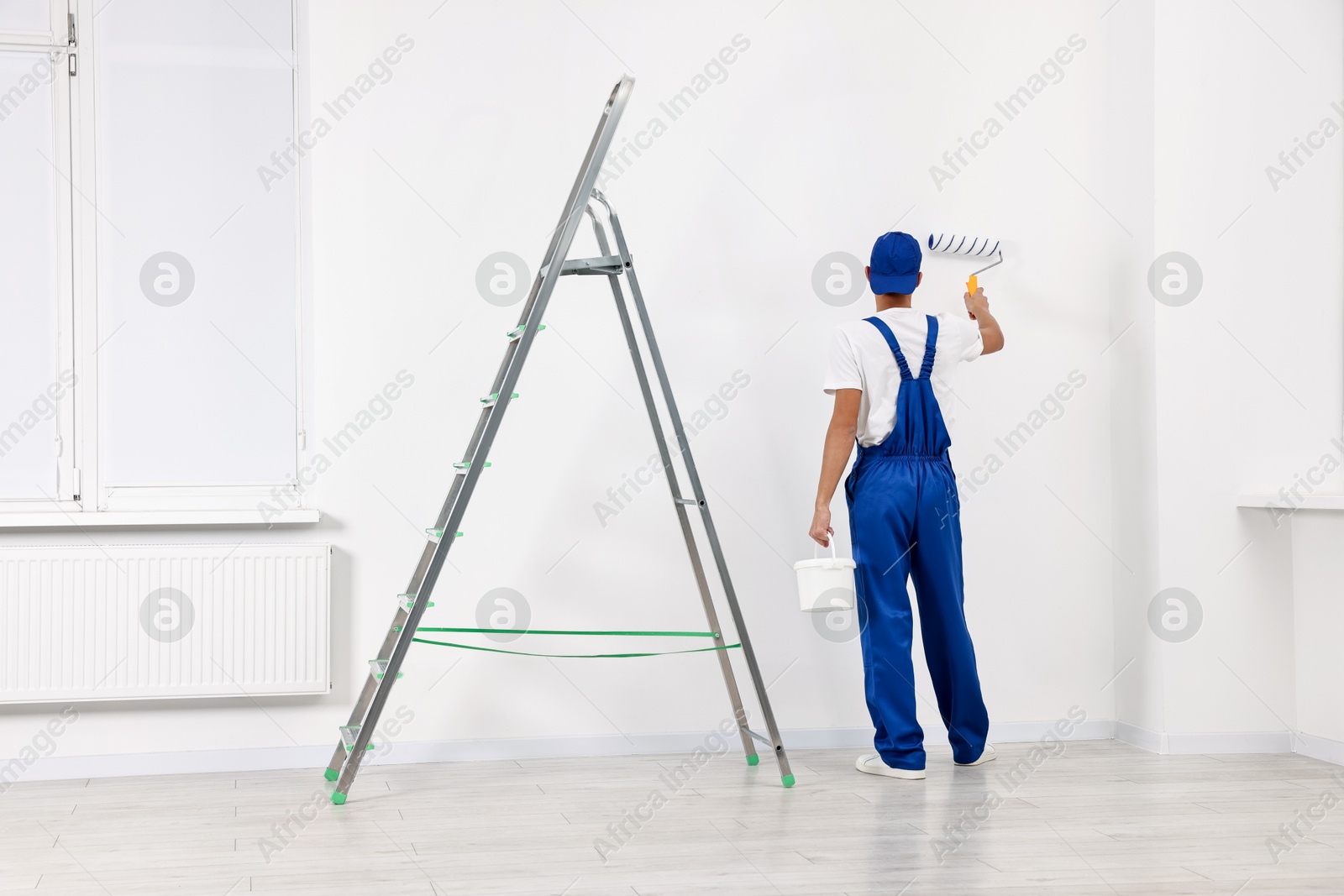 Photo of Male handyman painting wall with roller near ladder indoors, back view