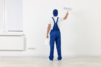 Photo of Male handyman painting wall with roller indoors, back view