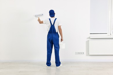 Photo of Male handyman painting wall with roller indoors, back view