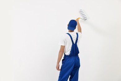 Photo of Male handyman painting wall with roller indoors, back view. Space for text