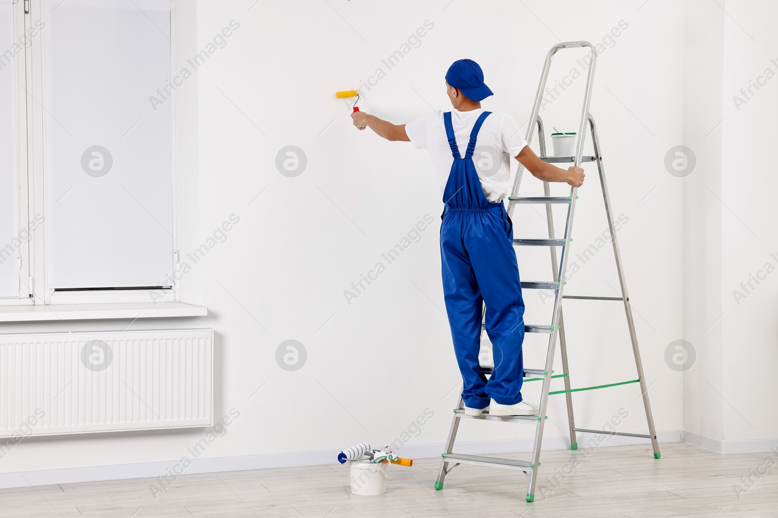 Photo of Male handyman painting wall with roller indoors, back view. Space for text