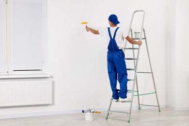 Photo of Male handyman painting wall with roller indoors, back view. Space for text