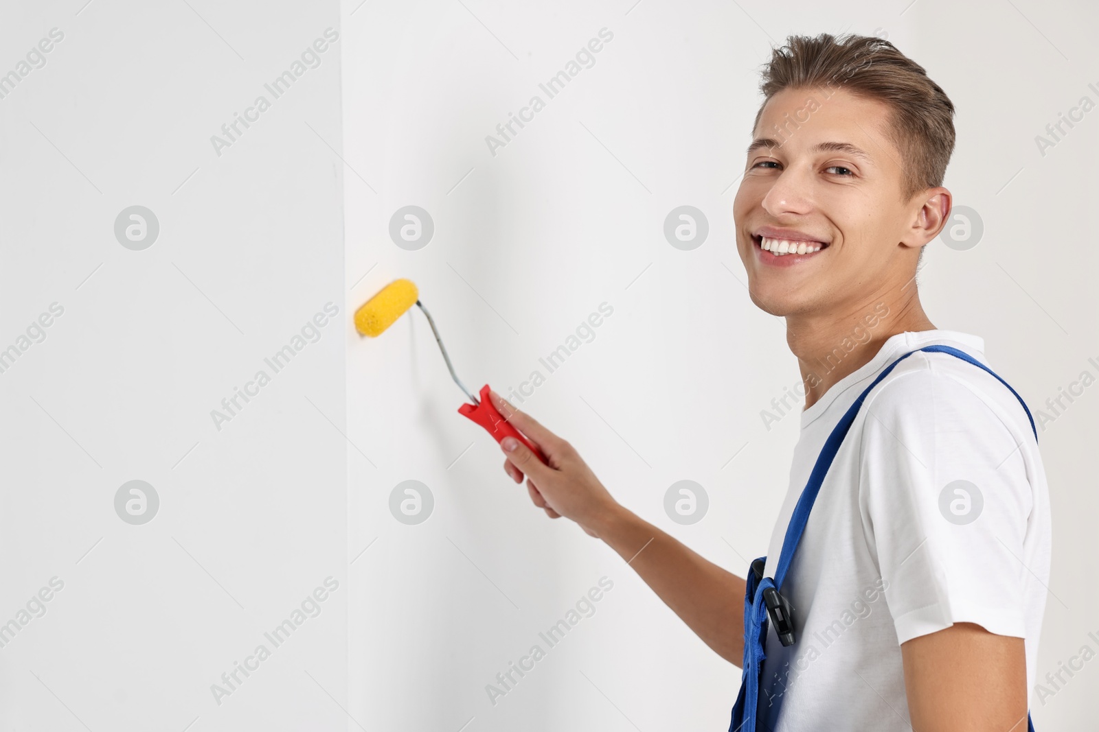 Photo of Smiling handyman painting wall with roller indoors. Space for text