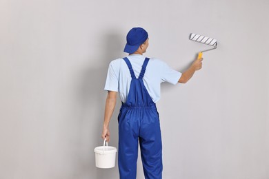 Photo of Male handyman painting wall with roller indoors, back view