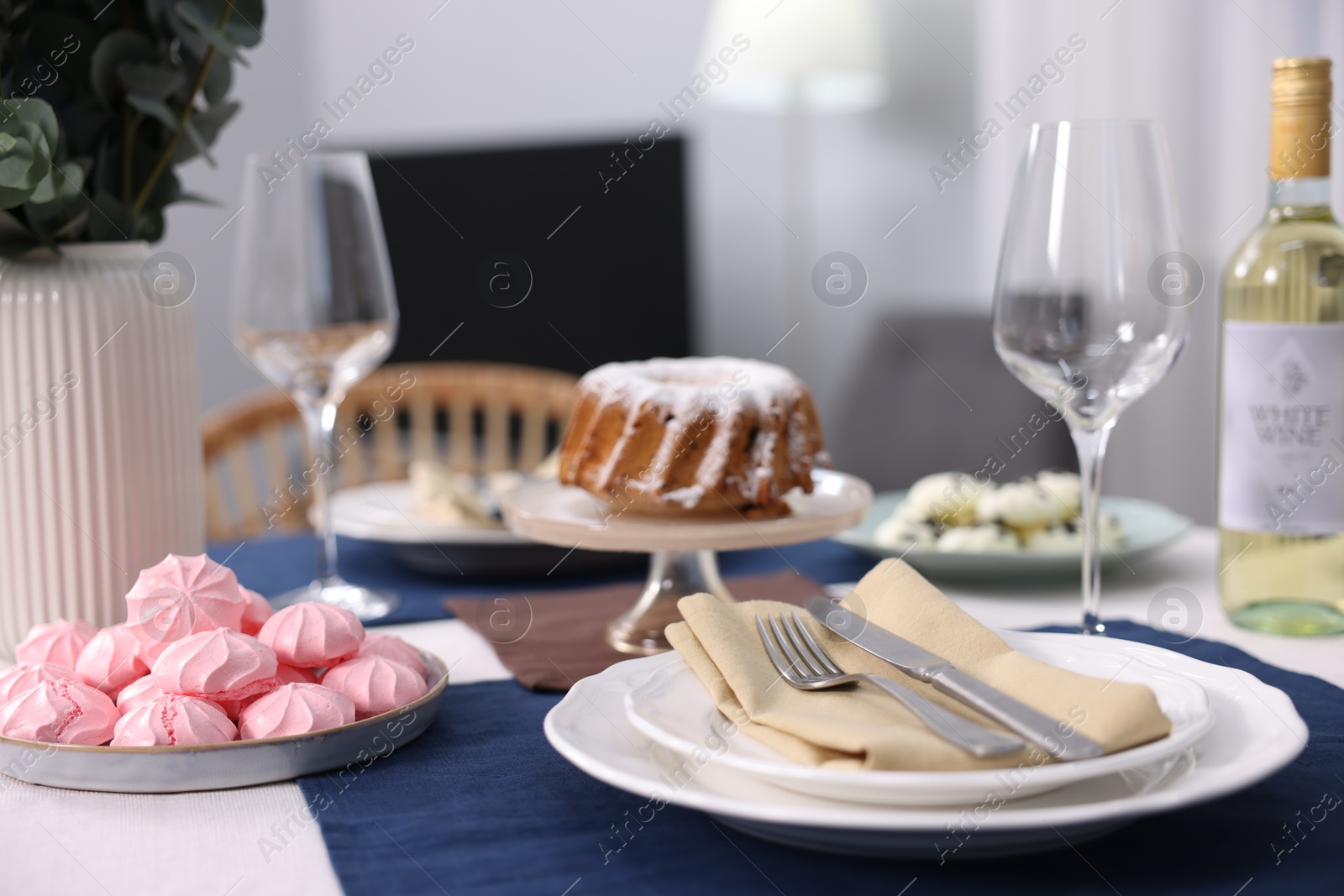 Photo of Festive table setting with dishware, desserts, wine and glasses indoors, closeup