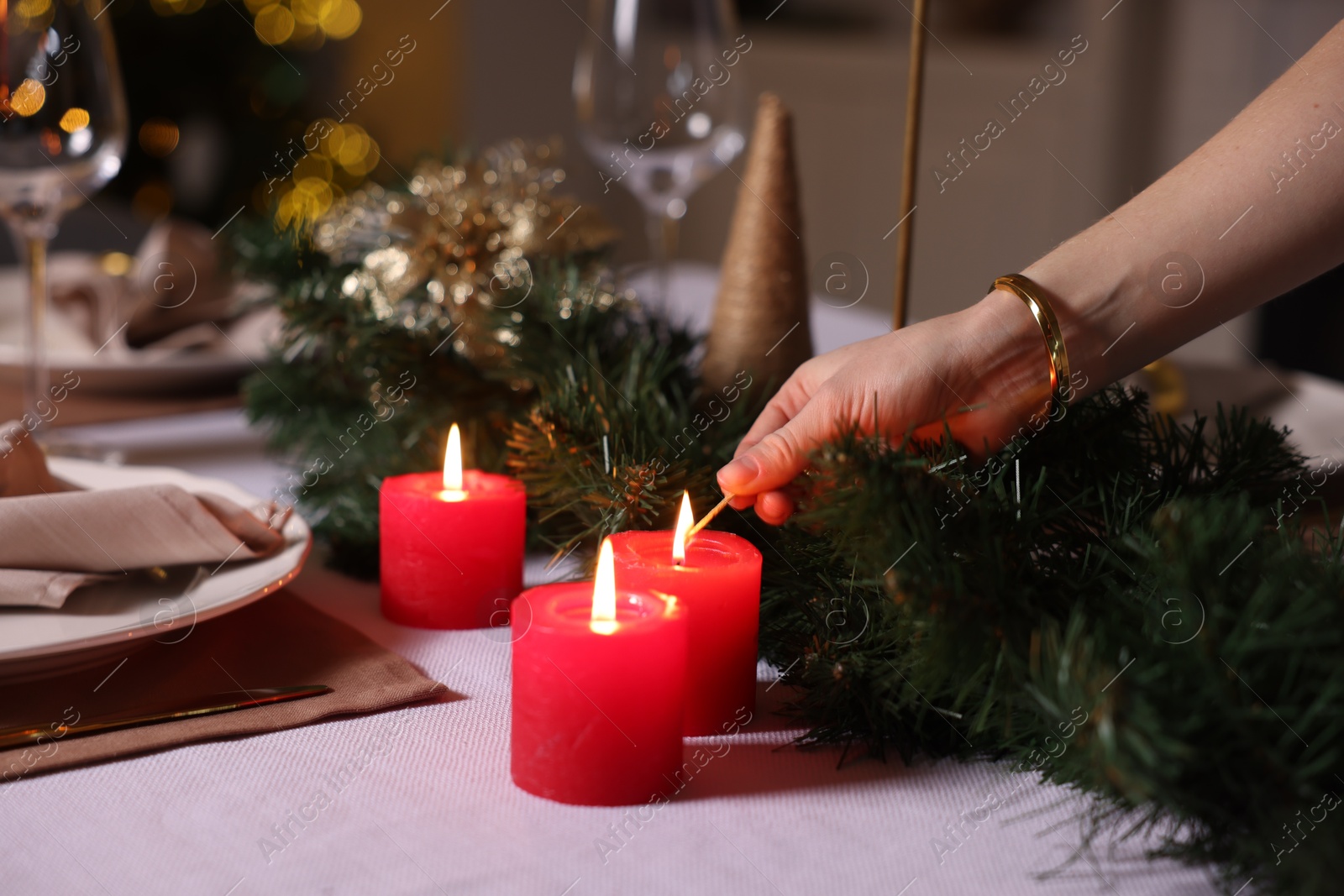 Photo of Woman lighting candle with match at table in room decorated for Christmas, closeup