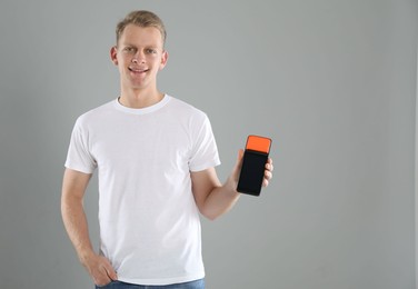 Photo of Happy young man with payment terminal on light grey background, space for text