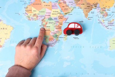 Photo of Woman pointing at world map with toy car, top view. Road trip