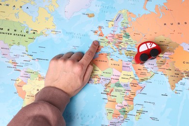 Photo of Woman pointing at world map with toy car, top view. Road trip