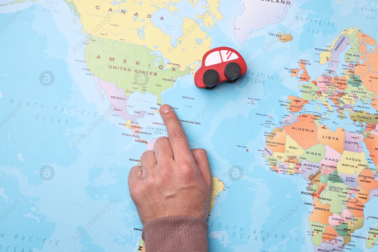 Photo of Woman pointing at world map with toy car, top view. Road trip