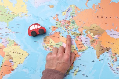 Photo of Woman pointing at world map with toy car, top view. Road trip