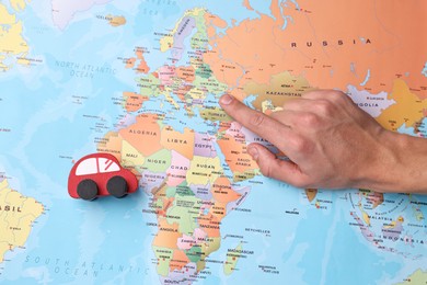 Photo of Woman pointing at world map with toy car, top view. Road trip