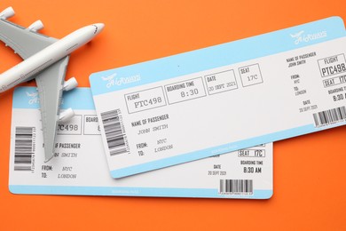 Photo of Travel agency. Flight tickets and plane model on orange background, flat lay