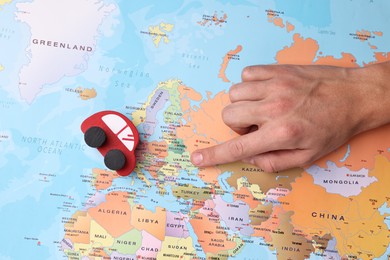 Photo of Woman pointing at world map with toy car, top view. Road trip