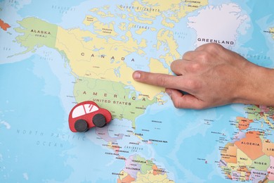 Photo of Woman pointing at world map with toy car, top view. Road trip