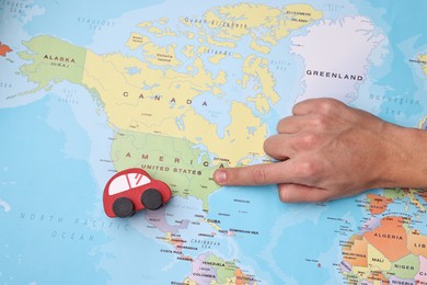 Photo of Woman pointing at world map with toy car, top view. Road trip