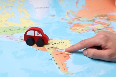 Photo of Woman pointing at world map with toy car, closeup. Road trip