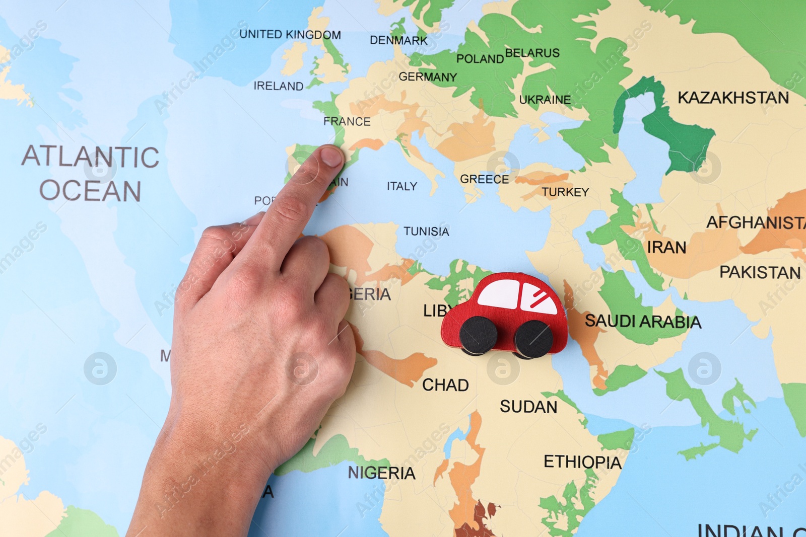 Photo of Woman pointing at world map with toy car, top view. Road trip