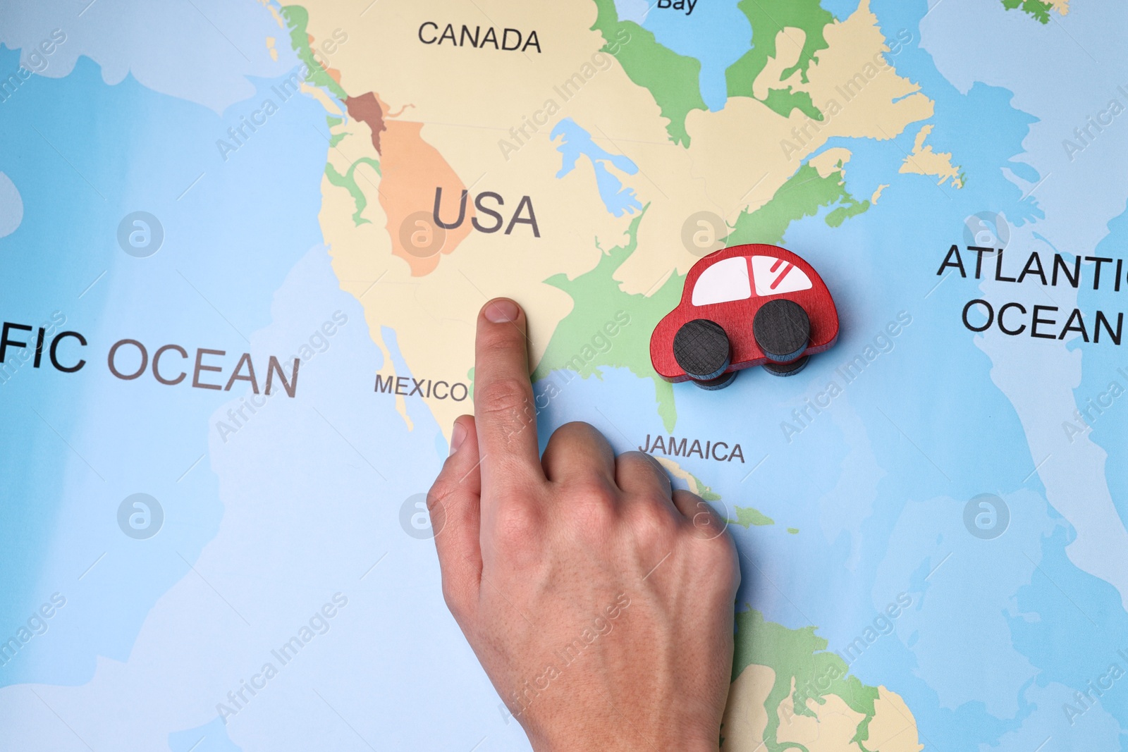 Photo of Woman pointing at world map with toy car, top view. Road trip