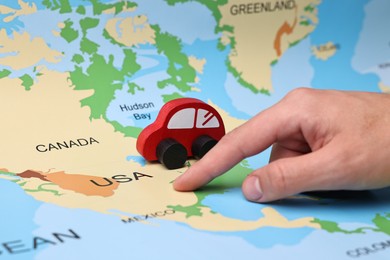 Photo of Woman pointing at world map with toy car, closeup. Road trip