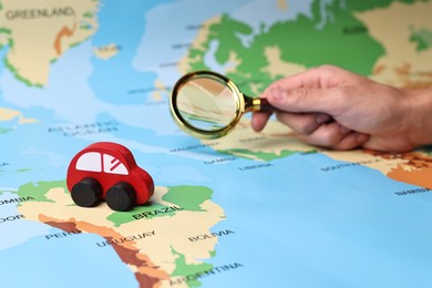 Photo of Woman looking at world map through magnifying glass, focus on red toy car. Road trip