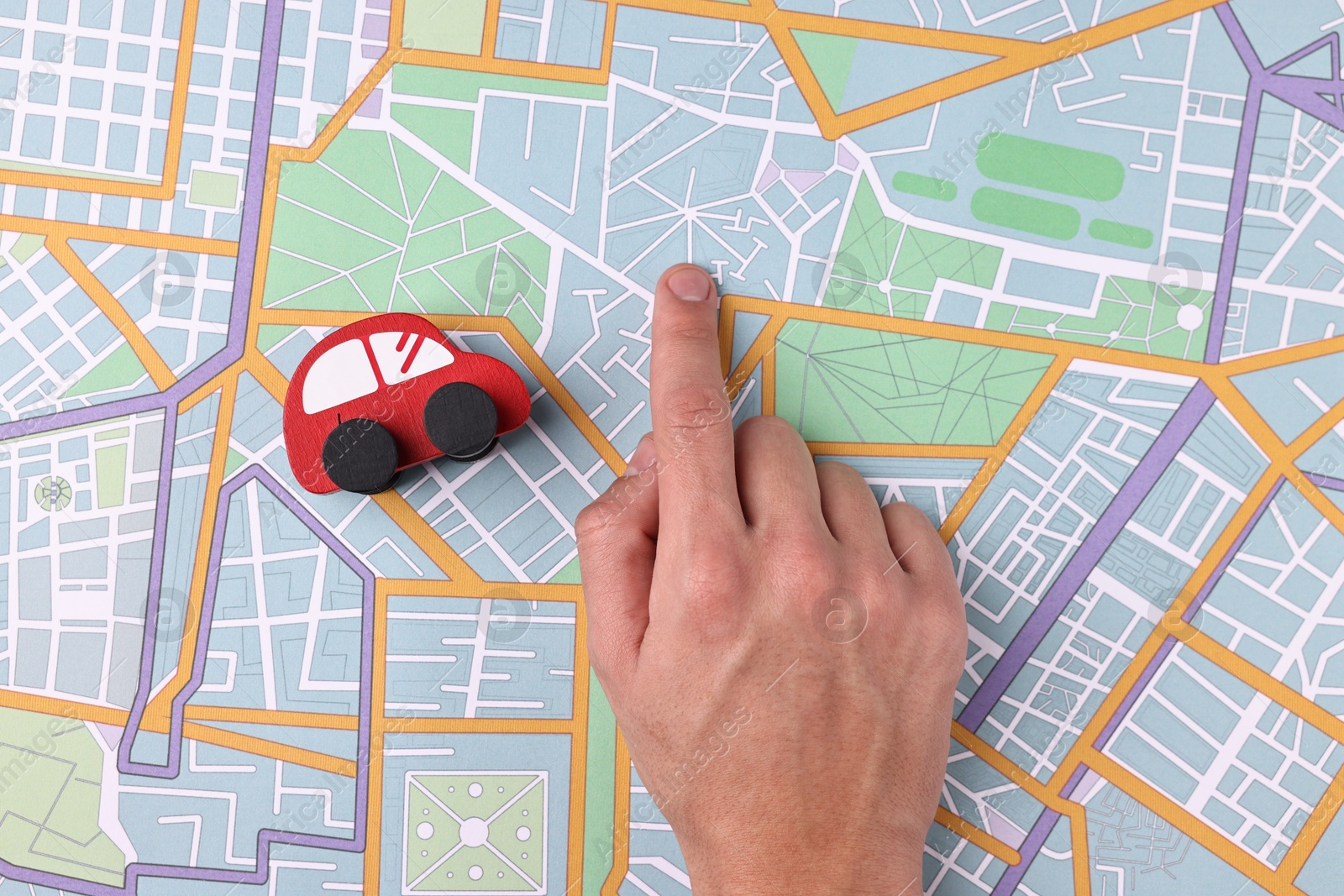 Photo of Woman pointing at city map with red toy car, top view. Road trip