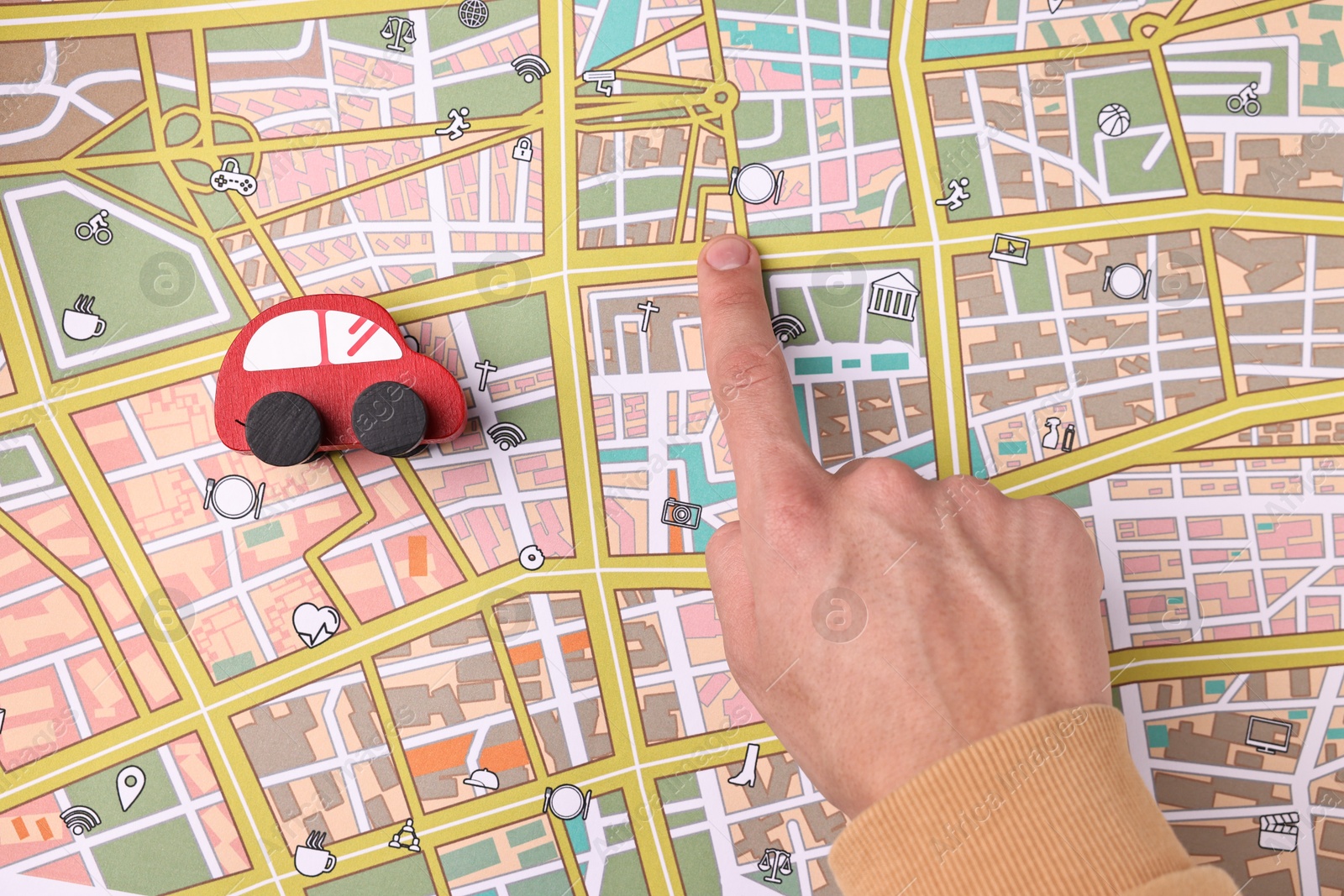 Photo of Woman pointing at city map with red toy car, top view. Road trip