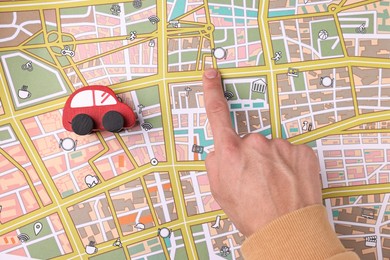 Photo of Woman pointing at city map with red toy car, top view. Road trip