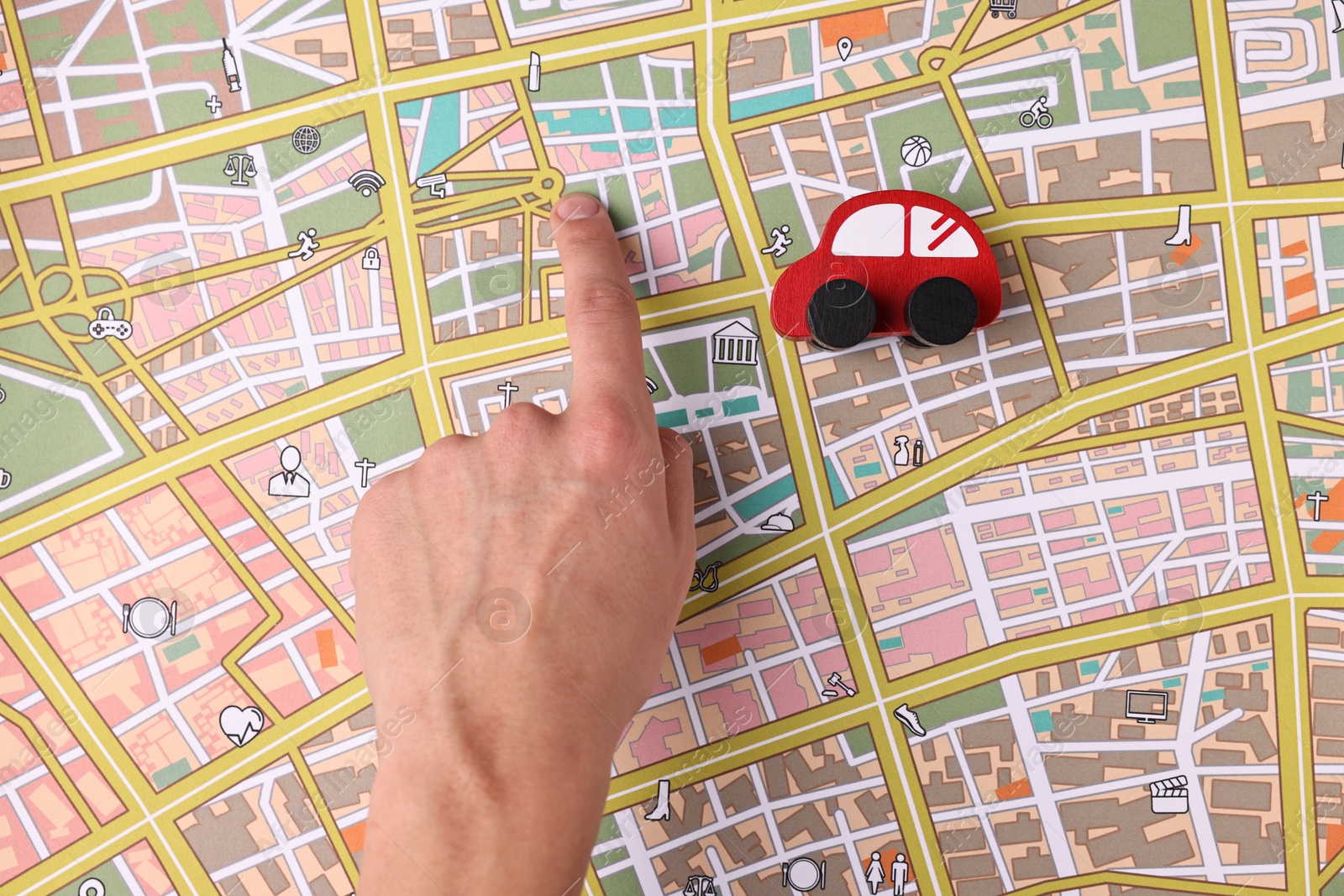 Photo of Woman pointing at city map with red toy car, top view. Road trip