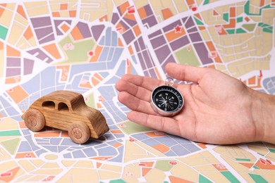 Photo of Woman holding compass on city map with wooden toy car, closeup. Road trip