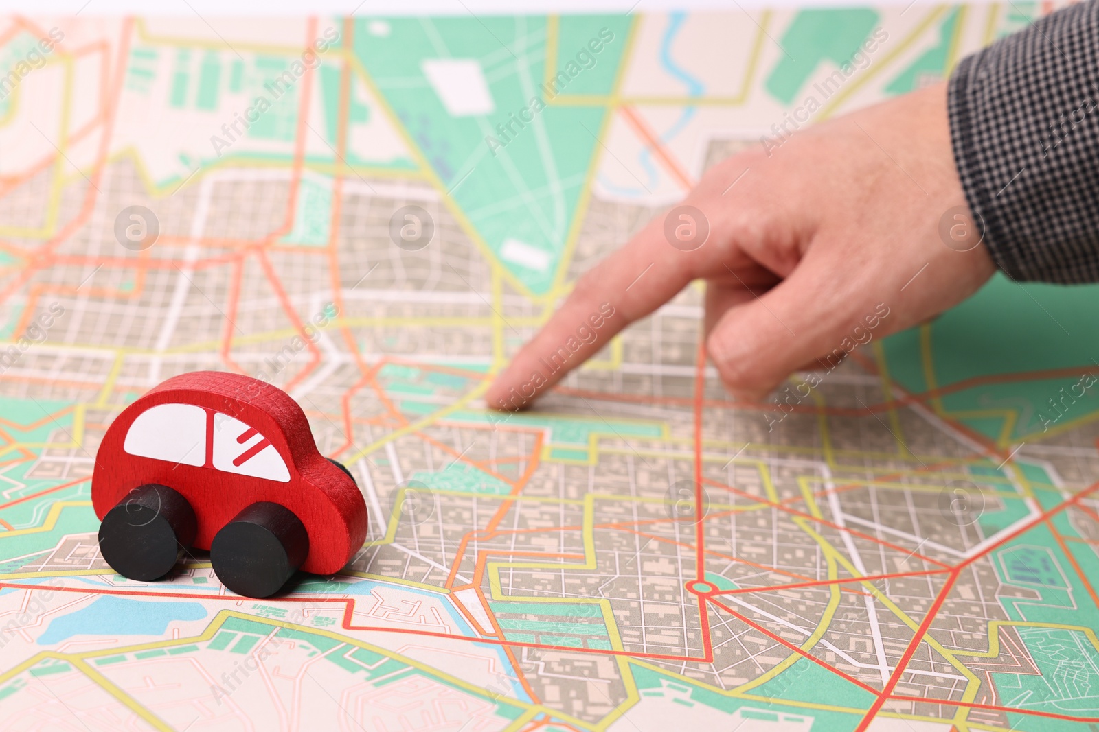 Photo of Woman pointing at city map with red toy car, closeup. Road trip