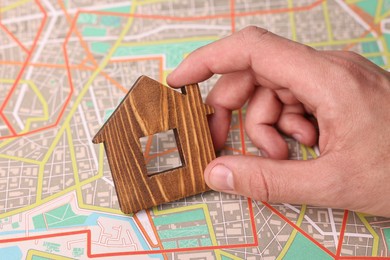 Photo of Woman holding wooden house model on city map, closeup. Accommodation search