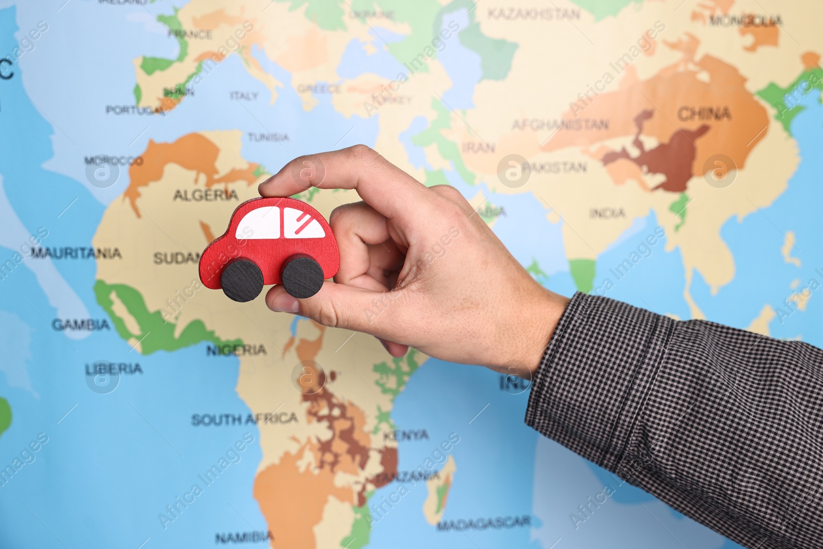 Photo of Woman holding red toy car near world map, closeup. Road trip