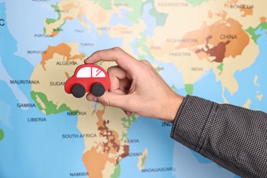 Photo of Woman holding red toy car near world map, closeup. Road trip