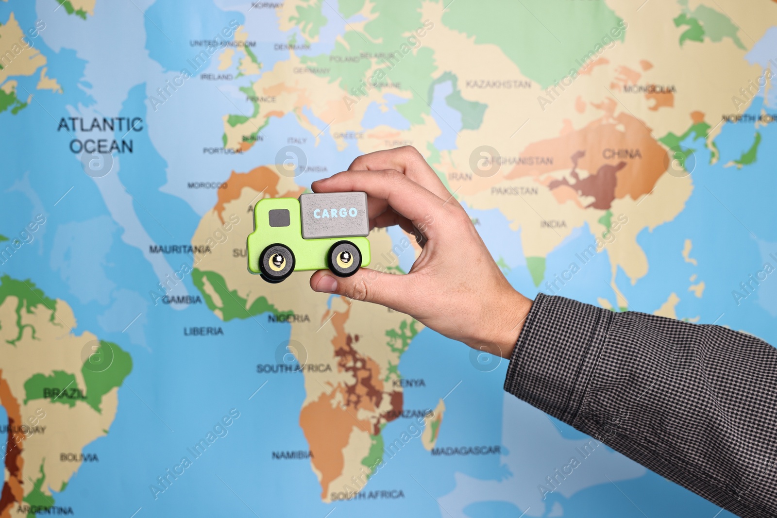 Photo of Woman holding toy truck near world map, closeup. Logistics concept